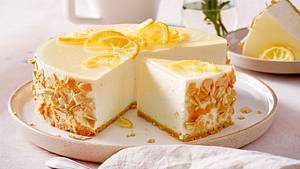 Hohe Zitronentorte ohne Backen aus Frischkäse, mit Eiswaffelboden und Zitronenscheiben-Dekoration auf einem hellen Teller mit kleinem Rand. - Foto: House of Food / Bauer Food Experts KG