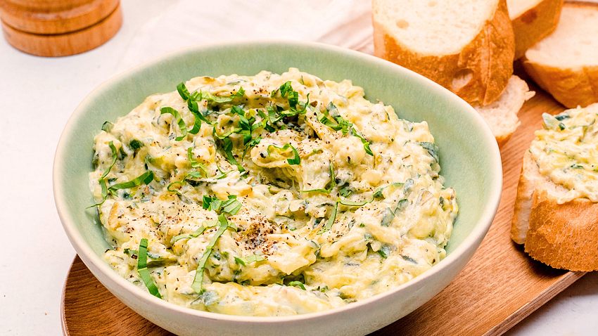 Zucchini-Aufstrich mit frischen Basilikumstreifen in einer Schale angerichtet. Mit Baguettescheiben.  - Foto: Show Heroes