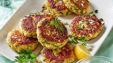 Zucchini-Frikadellen auf einem weißen, rechteckigen Teller mit Zitronenspalte und frischen Kräutern - Foto: House of Food / Bauer Food Experts KG