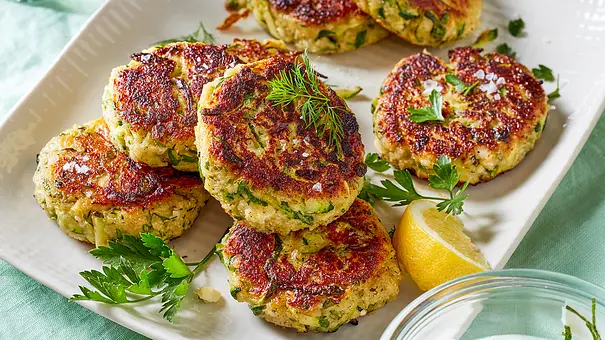 Knusprig gebraten Zucchini-Frikadellen liegen auf einer Servierplatte. Serviert werden sie mit frischen Kräutern, grobem Meersalz und Zitrone. - Foto: LECKER @ Bauer Media Group Knusprig gebraten Zucchini-Frikadellen liegen auf einer Servierplatte. Serviert werden sie mit frischen Kräutern, grobem Meersalz und Zitrone. - Foto: LECKER @ Bauer Media Group