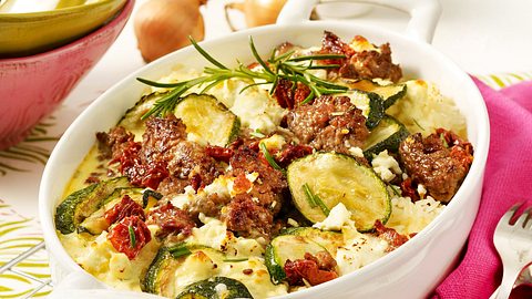Der Zucchini-Hackfleisch-Auflauf mit Feta und Reis befindet sich in einer weißen Auflaufform und ist mit einem Zweig Rosmarin garniert. - Foto: House of Food / Bauer Food Experts KG