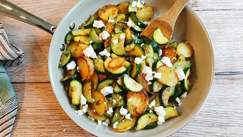 Zucchini-Kartoffel-Pfanne mit Feta bestreut rustikal auf einem Holztisch serviert. - Foto: LECKER @ Bauer Media Group / Birte Wloka