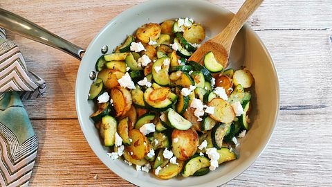 Zucchini-Kartoffel-Pfanne mit Feta bestreut auf einem Holztisch serviert. - Foto: LECKER @ Bauer Media Group / Birte Wloka
