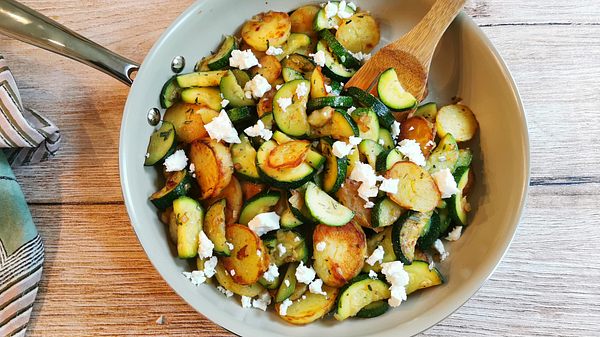 Zucchini-Kartoffel-Pfanne mit Feta bestreut rustikal auf einem Holztisch serviert. - Foto: LECKER @ Bauer Media Group / Birte Wloka